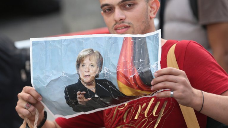 Млад бежанец държи снимка на Ангела Меркел при пристигането си на гарата в Мюнхен (Галерия)