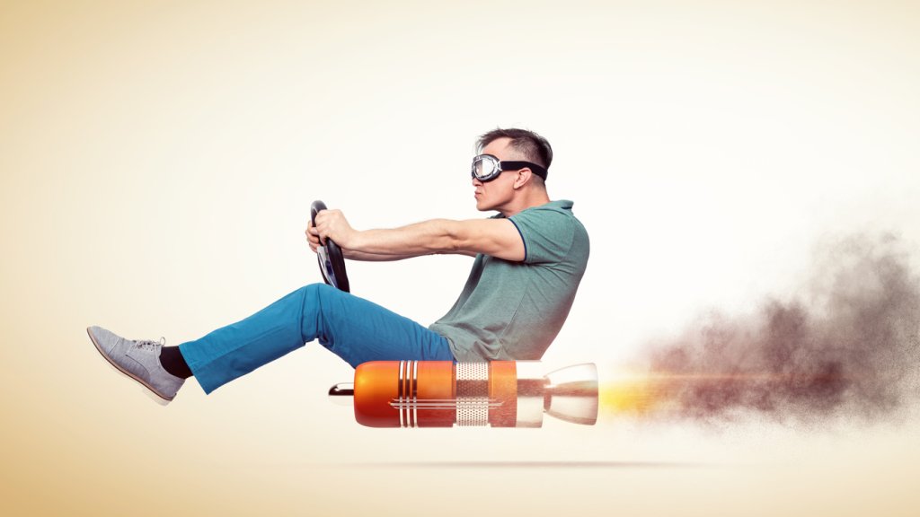 Cool man in casual clothes with goggles holds a steering wheel in his hands while driving an alternative vehicle, on yellow background.
