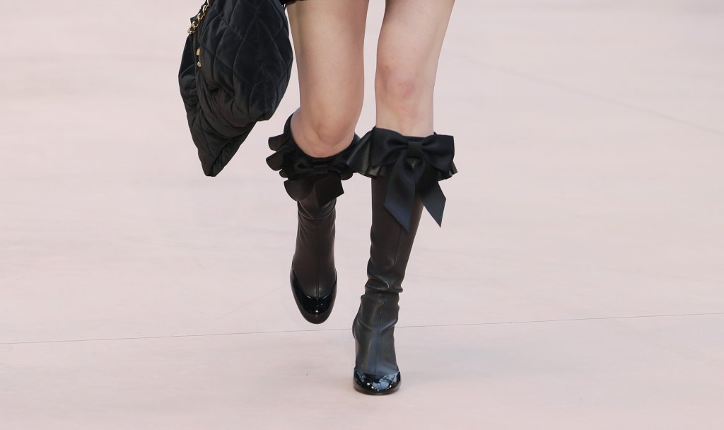 Нео-готика с градски характер
Зимата връща мрачното очарование при обувките, но без костюмната театралност. Високи ботуши, заострени форми и плътни материи създават усещане за готическа елегантност, пречупена през градския ритъм. Грубата кожа, дебелите подметки и леко „недоизпипаните“ детайли приземяват визията и я правят драматична, но поносима за ежедневието.