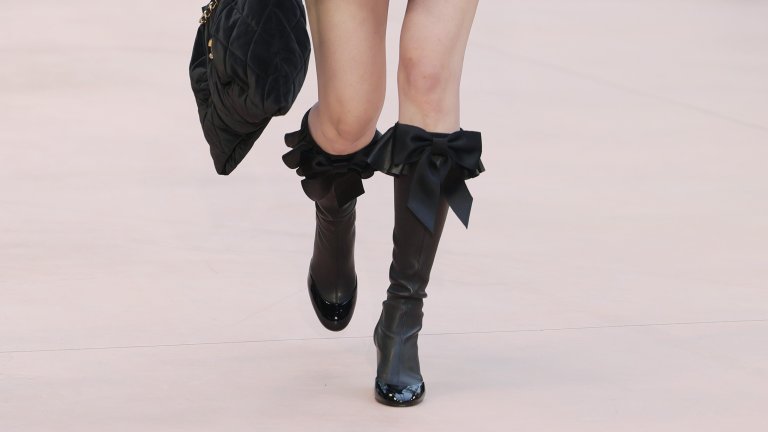 Нео-готика с градски характер
Зимата връща мрачното очарование при обувките, но без костюмната театралност. Високи ботуши, заострени форми и плътни материи създават усещане за готическа елегантност, пречупена през градския ритъм. Грубата кожа, дебелите подметки и леко „недоизпипаните“ детайли приземяват визията и я правят драматична, но поносима за ежедневието.