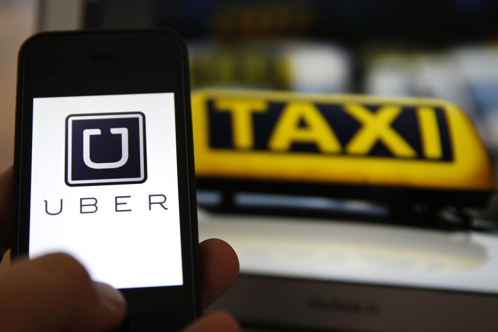 An illustration picture shows the logo of car-sharing service app Uber on a smartphone next to the picture of an official German taxi sign