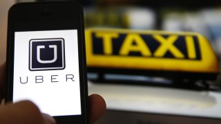 An illustration picture shows the logo of car-sharing service app Uber on a smartphone next to the picture of an official German taxi sign