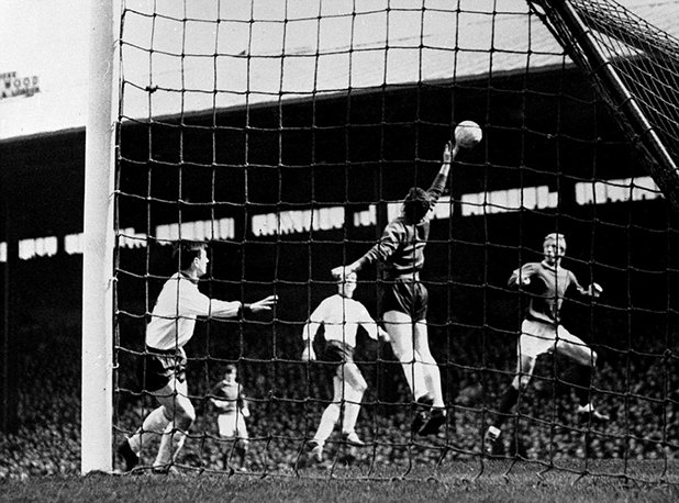 Мач от Първа дивзия на "Олд Трафорд" през април 1965-а. Денис Лоу, известен като Краля, стреля с глава, но топката минава над гредата на вратата на Ливърпул, пазена от Томи Лоурънс. Юнайтед печели с 3:0 по пътя си към титлата през този сезон под ръководството на Мат Бъзби. Сезонът е паметен и за Ливърпул, който вдига ФА къп за първи път с Бил Шенкли за мениджър на скамейката.