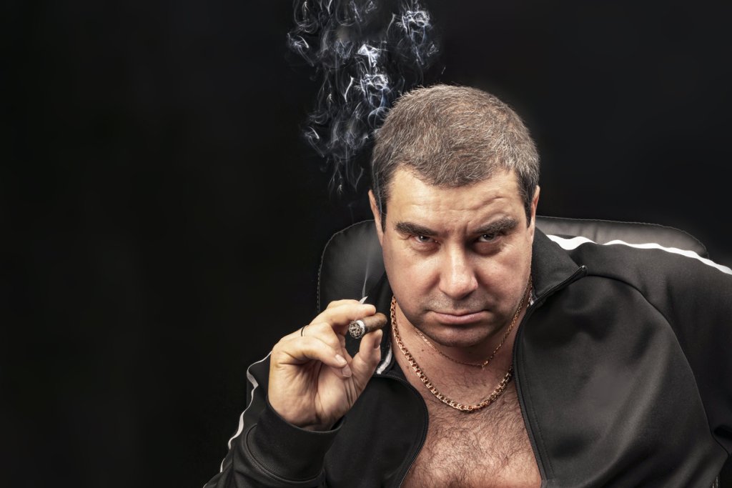 male portrait, a man Smoking a cigar. thug, experienced criminal Smoking a cigar sitting on a chair. Russian mafia. Plowman's in jail, don. copy space, black and gloomy background
