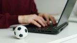 Young man reading soccer news or writing football article on laptop. Soccer ball on the table. Betting, gambling concept.