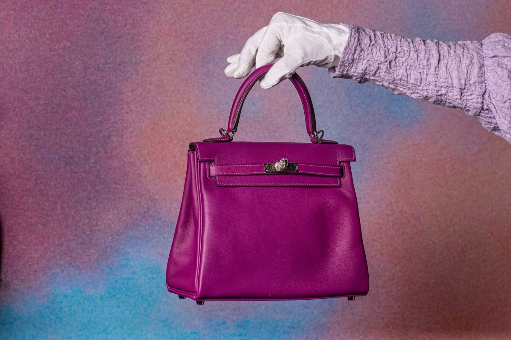 Kelly на Hermès
Историята на чантата Kelly започва през 1923 г., когато Емил-Морис Ерме (внук на основателя на Hermès) и дизайнерът Етор Бугати обмислят да разширят колекцията си с по-елегантен вид на популярните по това време пощенски чанти. Те трябва да са практични и в същото време семпли, така че да говорят за висша мода.
30 години след създаването им актрисата Грейс Кели получава една от тези чанти като подарък и я използва, за да скрие бременността си от фотографите. Снимките, в които прикрива заобленото си коремче с чантата на Hermès, заливат пресата и предизвикват силен интерес към аксесоара, заради което от бранда ѝ дават официално името Kelly.