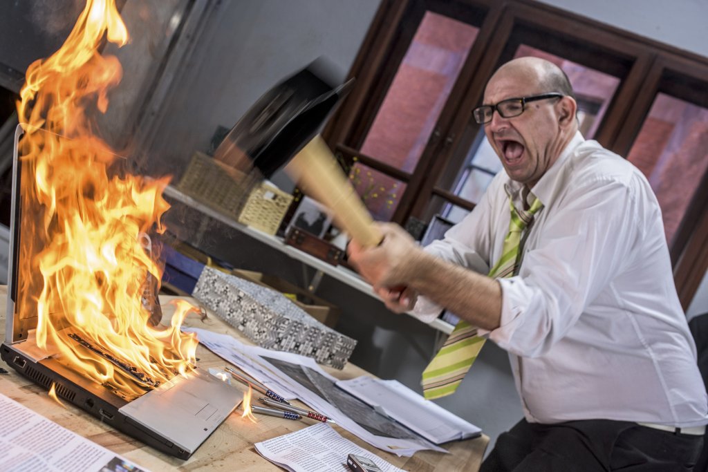 Mature adult businessman smashing laptop on fire with hammer