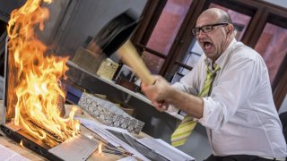 Mature adult businessman smashing laptop on fire with hammer