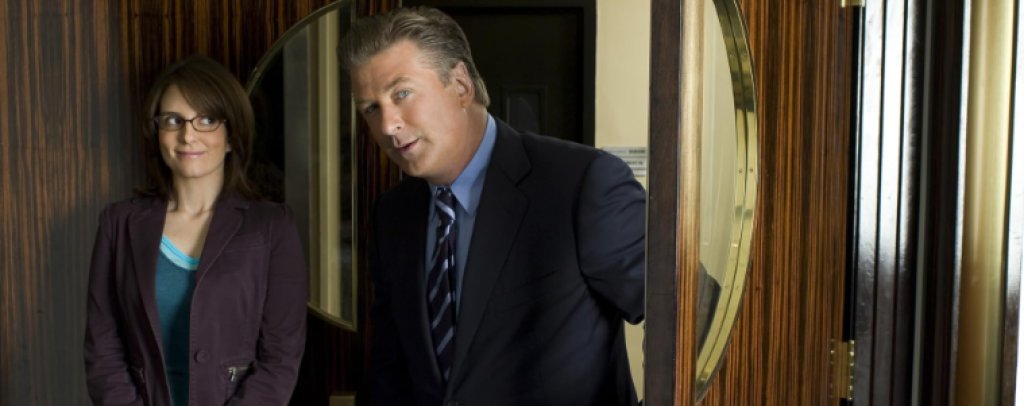 8. 30 Rock / „Рокфелер плаза 30“ (2006–2013)
Опитът на Тина Фей като главен сценарист на Saturday Night Live се превръща в основа за една от най-бързите и гъсто населени с шеги телевизионни комедии.
Фей играе Лиз Лемън, която ръководи сценарния екип на скечово шоу. Работният ѝ ден минава между капризите на звездите, проблемите на колегите и намесата на корпоративния началник Джак Донаги, изигран от Алек Болдуин.
„Рокфелер плаза 30“ превръща телевизията в работно място, където творческите амбиции постоянно се сблъскват с рейтинги, реклама и нечие огромно его. Седемте сезона предлагат сатира на индустрията, която добре познава собствените си абсурди и с готовност ги използва за следващата шега.
