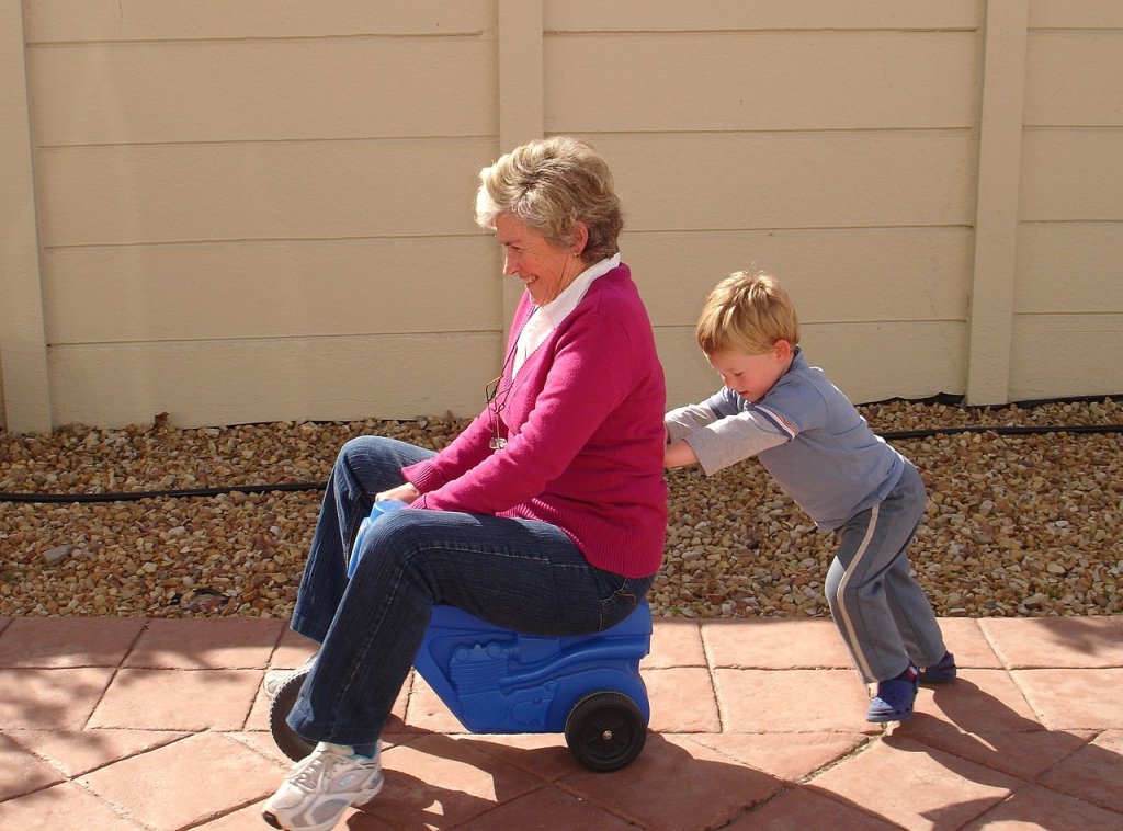 1280px-Child_pushing_grandmother_on_plastic_tricycle