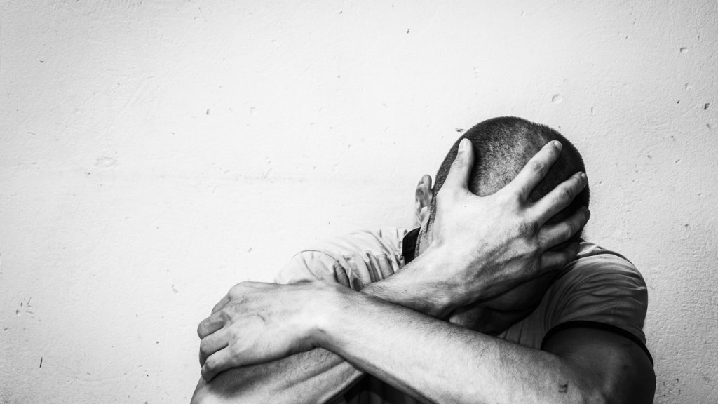 Homeless man drug and alcohol addict sitting alone and depressed on the street feeling anxious and lonely, social documentary concept black and white