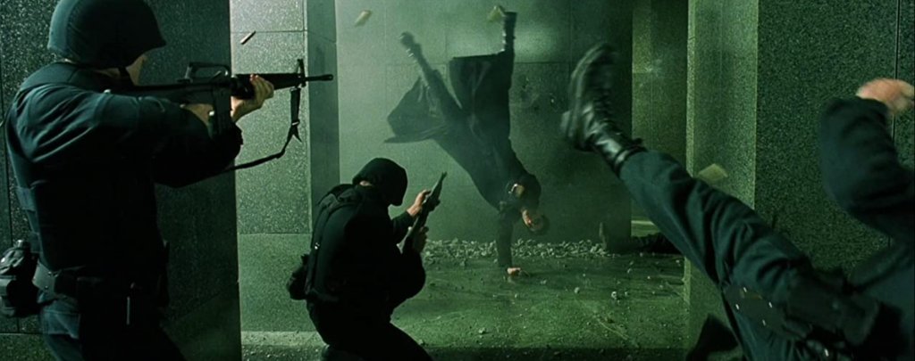 “Матрицата” - Престрелката във фоайето
“Матрицата” е толкова революционен и запомнящ се филм, че практически всеки един момент от него е велик сам по себе си. Това важи особено много за екшън сцените, които правят истинска революция в киното заради въвеждането на цял куп нови визуални ефекти.
Един от запомнящите се моменти, освен ръкопашните схватки, е престрелката във фоайето на бизнес сградата, когато Нео и Тринити отиват да спасят Морфей от плен. В нито един момент двамата не изглежда да бъдат в опасност, а целият акцент е поставен върху абсолютното им превъзходство над охраната на фона на пороя от олово и падащи отломки. Всичко това е заснето с няколко подхода на забавения кадър, които после започват да бъдат широко прилагани и в други филми.