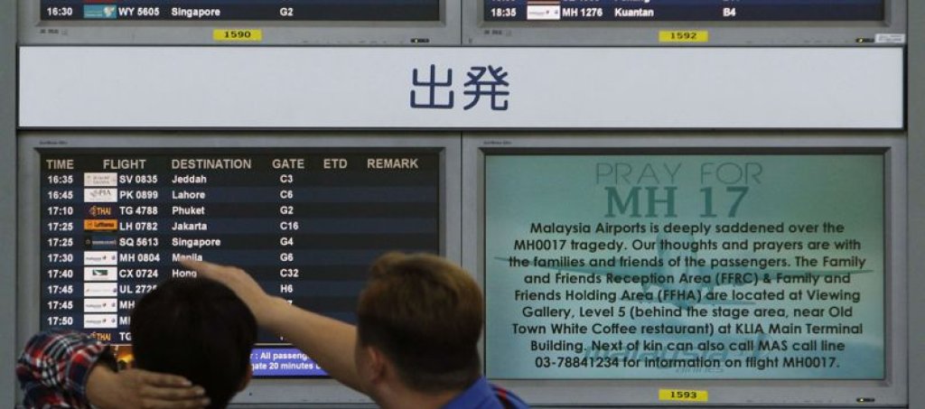Bystanders look at board displaying flight information and "Pray for MH17" message at Kuala Lumpur International Airport in Sepang