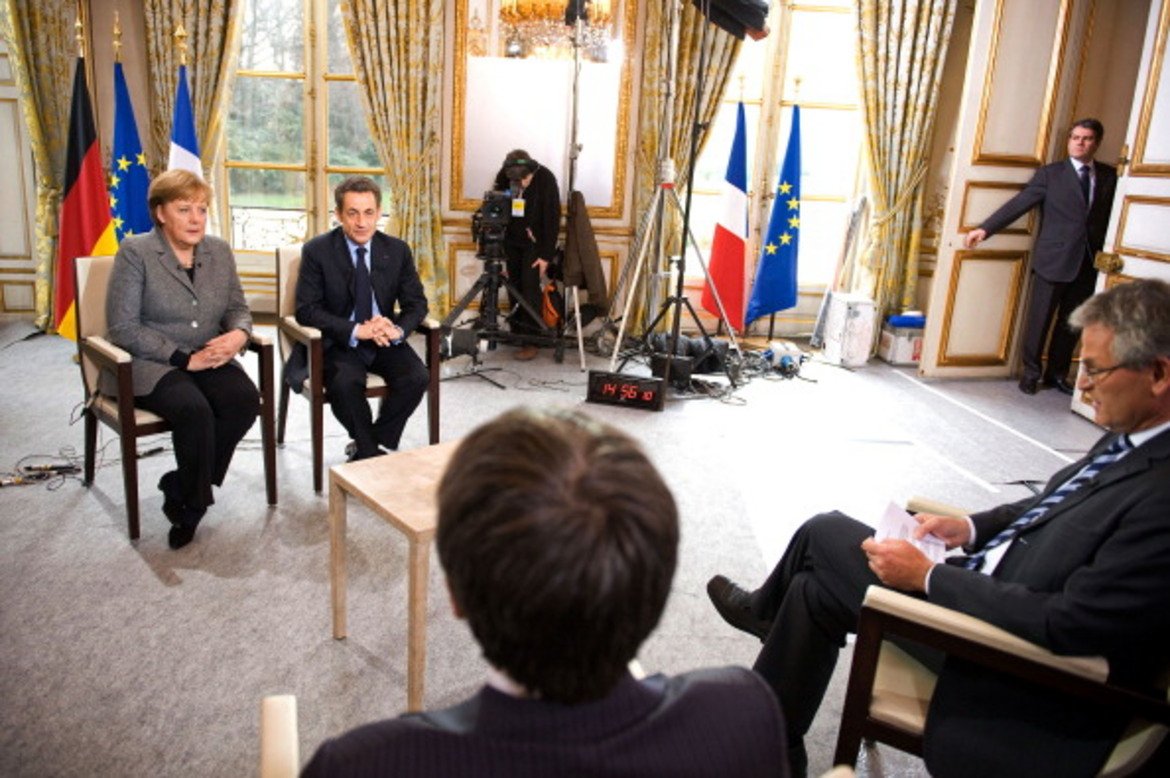 Пюжадас (в гръб) прави интервю на Ангела Меркел и Никола Саркози заедно с германски колега 