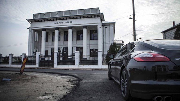 На входа на градчето стои къщата на Дан Финуту. Пред нея е паркирано новото му Порше