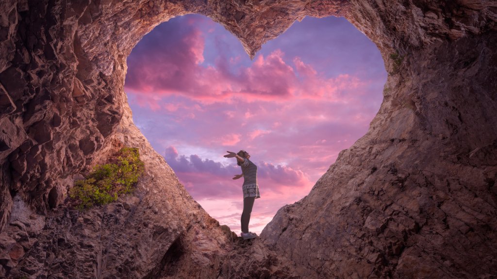 Young woman in heart shape cave towards the beautiful sky