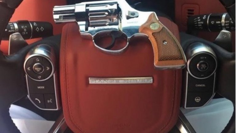 Сребърен револвер поставен върху волана на луксозен Range Rover