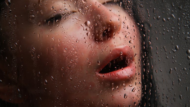 Girl with her mouth open behind wet glass