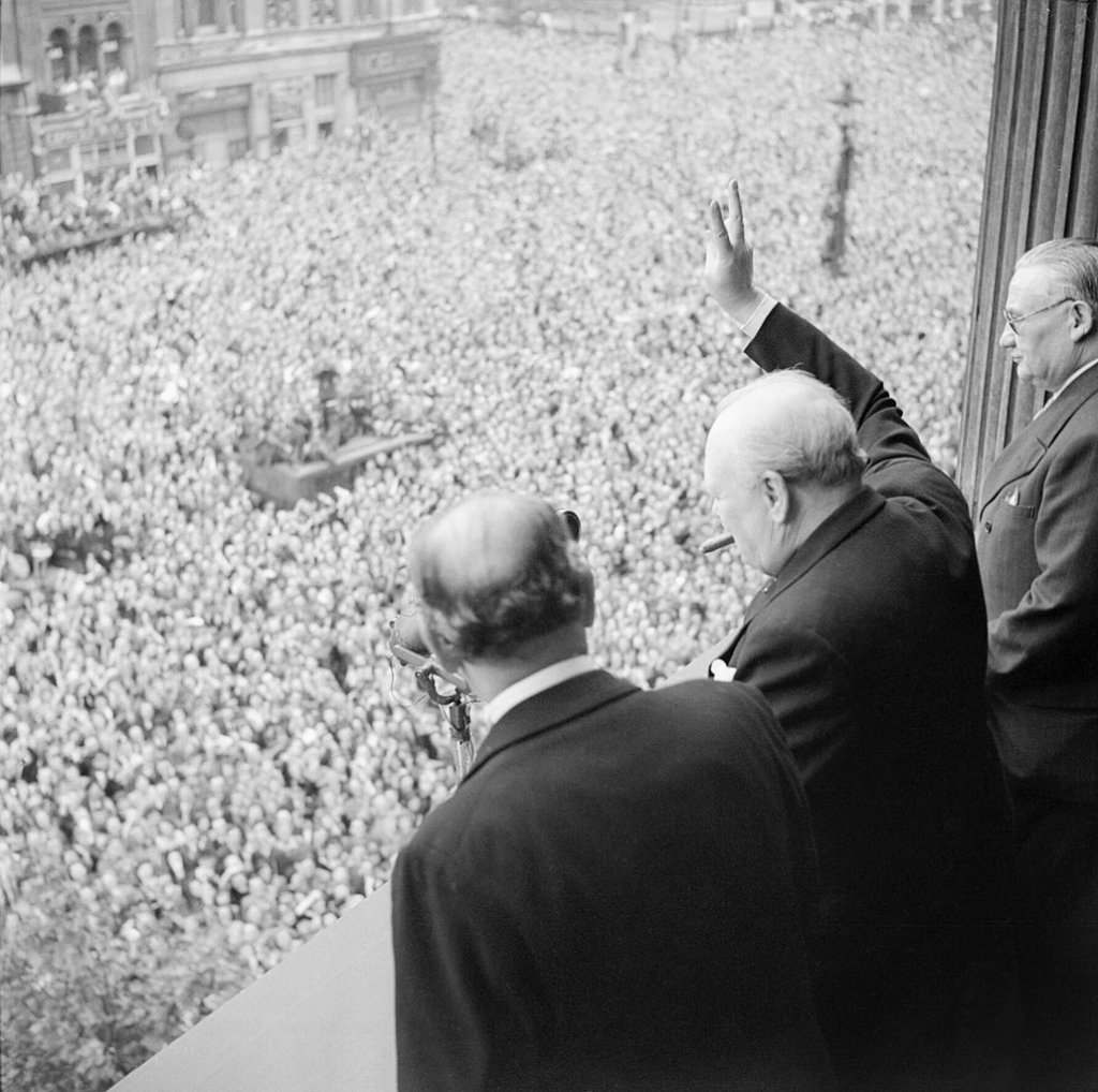 1030px-Winston_Churchill_waves_to_crowds_in_Whitehall_in_London_as_they_celebrate_VE_Day,_8_May_1945._H41849