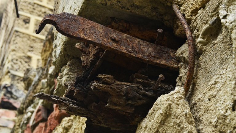 Метална скоба, която някога е придържала дървените греди на покрива, стърчи от изтърбушената стена