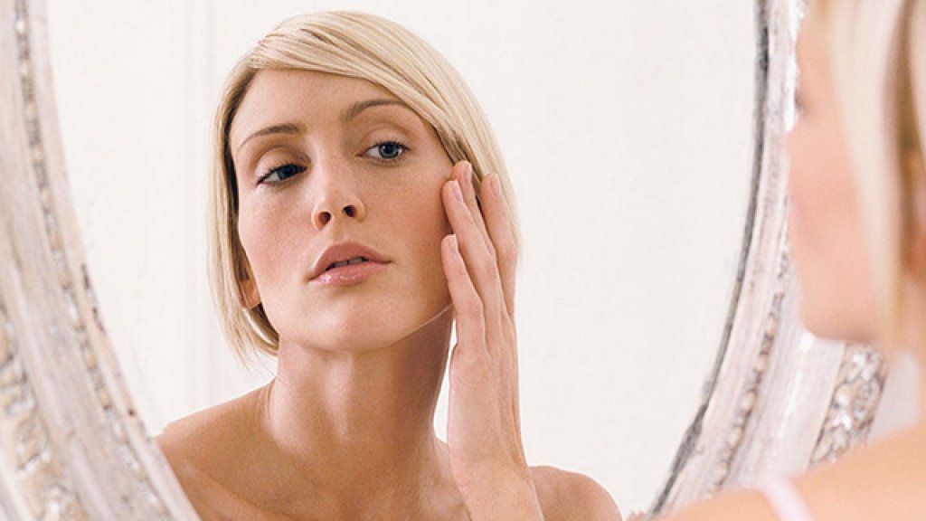 Young-woman-looking-in-mirror-hand-to-face