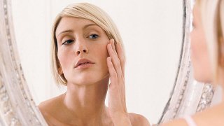 Young-woman-looking-in-mirror-hand-to-face