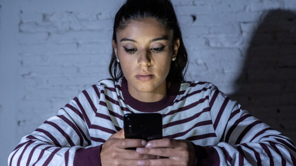 Frightened teenager or young woman using smart mobile cell phone as internet cyberbullying by message stalked abused victim.