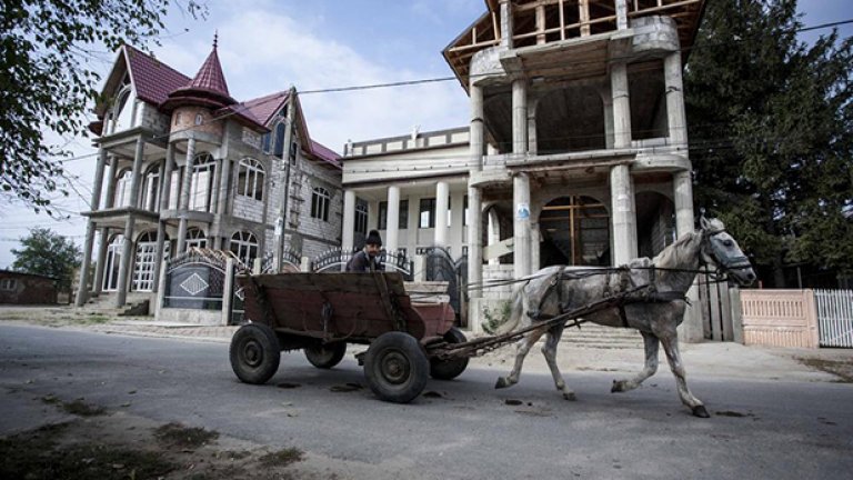 Мъж с каруца минава покрай две недовършени къщи. Жителите на градчето инвестират много от парите си в тези палати, като често им се налага да вземат пари назаем от роднините си. Понякога построяването на къщите отнема доста години