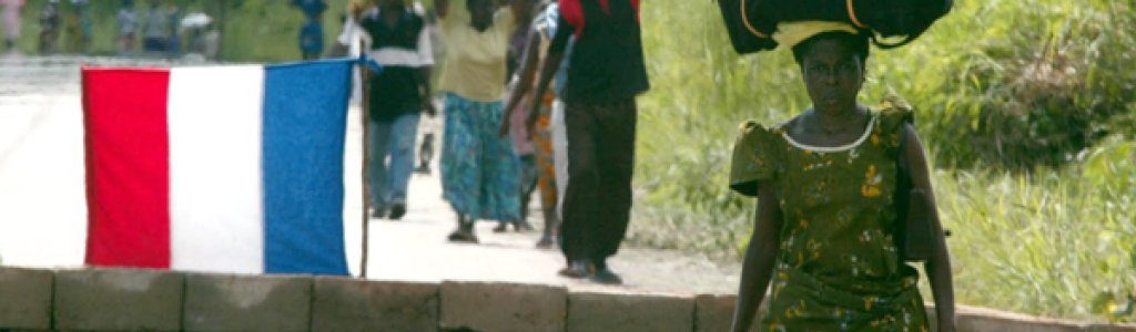 People fleeing from Bouake carry their possessions on their heads as they walk past a French army ch..