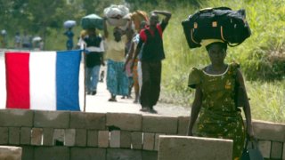 People fleeing from Bouake carry their possessions on their heads as they walk past a French army ch..
