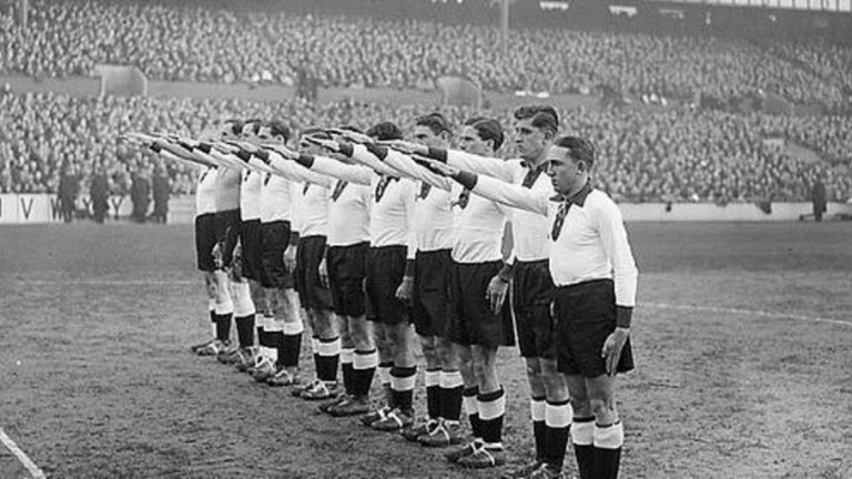 1935: „Хайл Хитлер!” в Лондон

За Адолф Хитлер най-важното спортно събитие се явяват олимпийските игри в Берлин през 1936 г. Но година по-рано един обикновен приятелски мач между Англия и Германия в Лондон „взривява“ страстите. Срещата трябва да се играе на стадиона на Тотнъм „Уайт Харт Лейн”, в средата на еврейския квартал. Сега е моментът Хитлер да организира антисемитистка демонстрация на стадиона. За целта от Германия са изпратени повече от 5000 души, членове на казионната организация „Kraft durch Freude”. Те развяват знаменца с пречупения кръст, докато двата отбора излизат на терена. Там, при построяването, германските футболисти отдават нацисткия поздрав „Хайл Хитлер!” с вдигнатата ръка. Евреите, присъстващи на мача, ги освиркват. В крайна сметка, идеята за пропагандиране на силата на арийския футбол пропада, тъй като Англия бие с 3:0.
