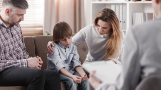 Mother hugging her autistic son, sitting next to a father during a family therapy