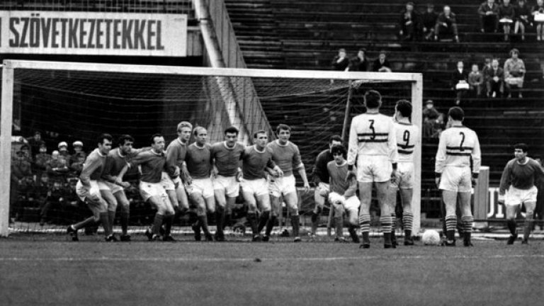 6 юни 1965 г. - Европейски приключения.
Флориан Алберт и Дежо Новак от Ференцварош мислят как да преодолеят стена от целия тим на Юнайтед в реванша  от полуфиналите на Купата на панаирните градове. "Червените дяволи" бият с 3:2 у дома, но губят с 0:1 в Унгария. Тогава правило за голове на чужд терен няма, та се налага 10 дни по-късно Юнайтед пак да пътува за Будапеща в трети мач. И отново губи. Европейската слава ще почака.
На снимката, от ляво на дясно: Джон Конъли, Шей Бренън, Ноби Стайлс, Денис Лоу, Боби Чарлтън, Били Фоулкс, Пат Креранд, Дейвид Херд, Джордж Бест, вратарят Пат Дън и Тони Дън.