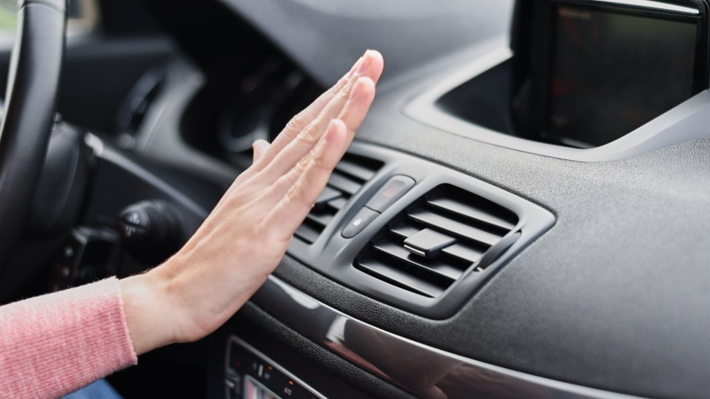 Woman hand on air conditioner ventilation grille in the car. Climate control panel