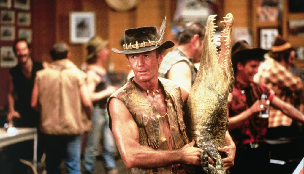 Crocodile Dundee / ”Дънди крокодила”
Тук вече говорим за величие, което нарежда филма в категорията “национално богатство” на Австралия, наред “Лудия Макс”, разбира се. Едва ли ще е преувеличено, ако кажем, че именно историята за Дънди е в основата на затвърждаването на всеки един възможен стереотип за Австралия. Филмът разказва за коравия Майкъл Дънди, който живее в австралийската пустош, а основното му занимание е да лови крокодили с голи ръце и да се напива до припадък. Всичко обаче се променя, когато се среща с една американска журналистка и заминава с нея за Ню Йорк.