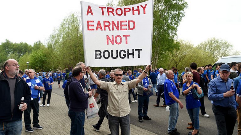 "Трофей, който е заслужен, а не купен".Плакатът казва всичко. Лестър, затънтен някъде около средата в скалата на финансовата мощ на английския футбол, изпревари акулите на бизнеса и модерния футбол.