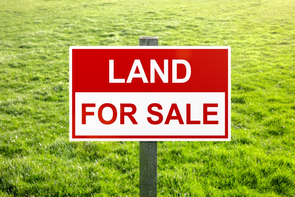 Land for sale sign in green grass field for housing development and construction