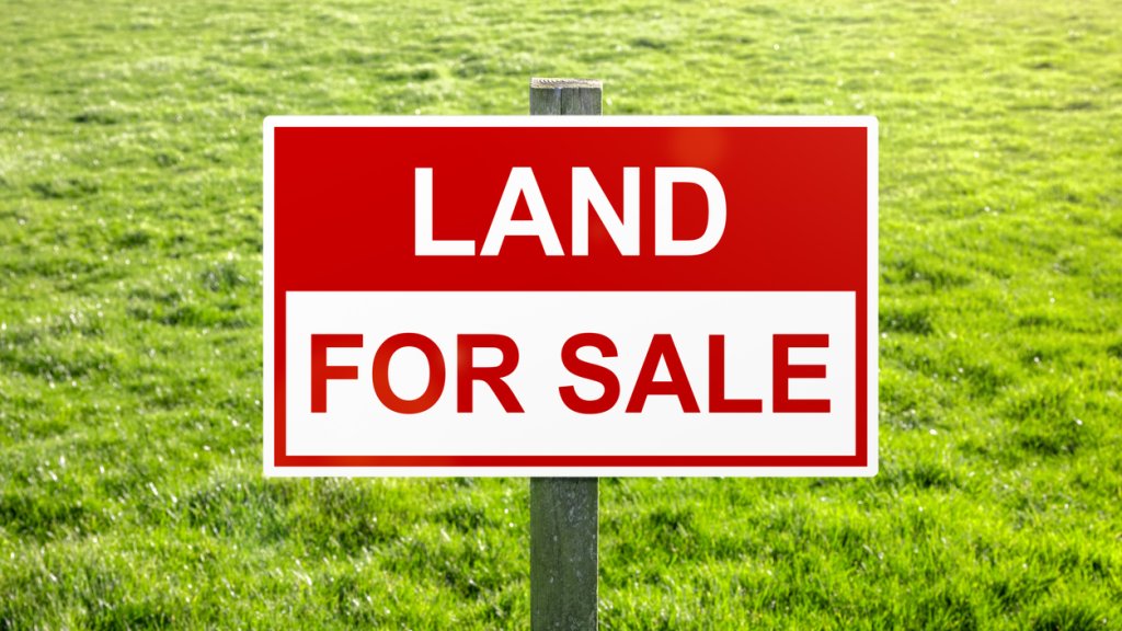 Land for sale sign in green grass field for housing development and construction
