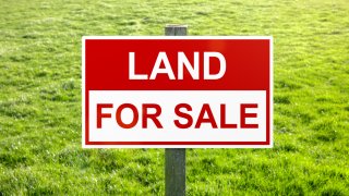 Land for sale sign in green grass field for housing development and construction