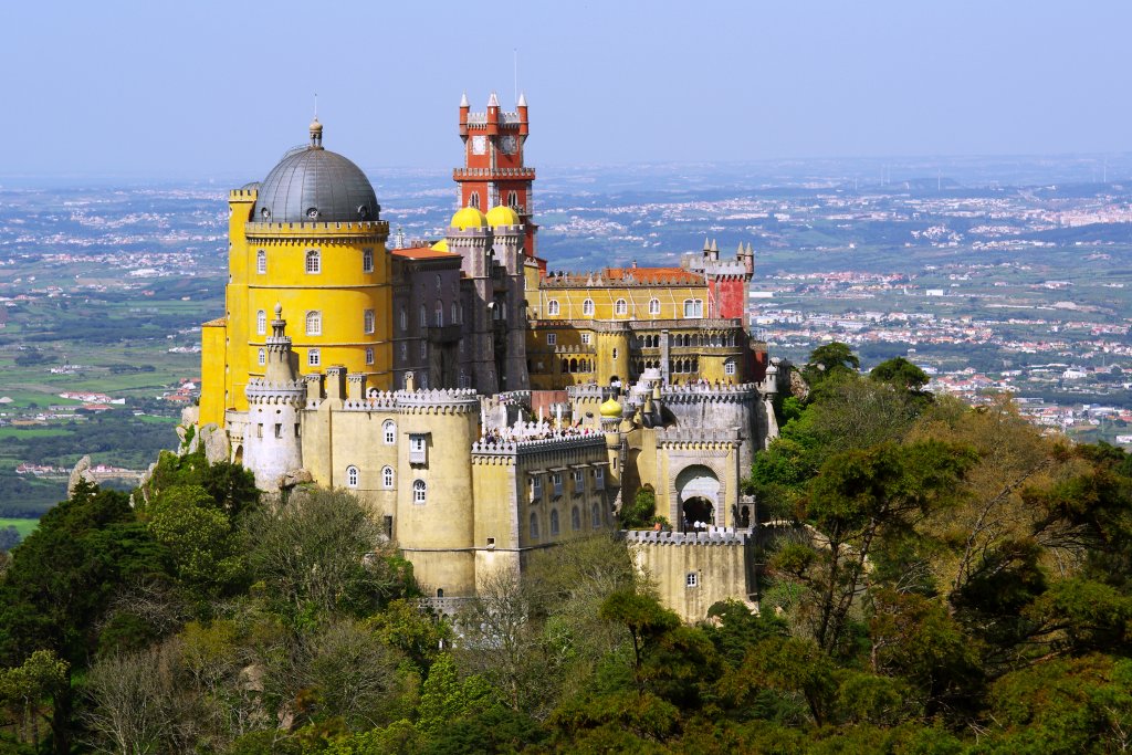 Дворецът Пена, Синтра
Може би най-известното място за посещения в Португалия, дворецът Пена в Синтра край Лисабон неслучайно напомня на приказния Нойшванщайн – той е вдъхновен и от германската романтична архитектура. Затова и прилича на замък от филм на Дисни, особено с ярките си, цветни кули и стени. 
В построения от крал Фердинанд II в средата на XIX век замък обаче се усещат и типичните за района влияния от Северна Африка. Околните гори придават на Пена и доза мистика и допълнително усещане за романтика.