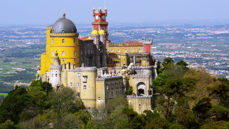 Дворецът Пена, Синтра
Може би най-известното място за посещения в Португалия, дворецът Пена в Синтра край Лисабон неслучайно напомня на приказния Нойшванщайн – той е вдъхновен и от германската романтична архитектура. Затова и прилича на замък от филм на Дисни, особено с ярките си, цветни кули и стени. 
В построения от крал Фердинанд II в средата на XIX век замък обаче се усещат и типичните за района влияния от Северна Африка. Околните гори придават на Пена и доза мистика и допълнително усещане за романтика.
