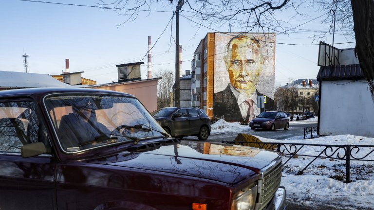 Мъж преминава с автомобила си Лада Рива 2107 покрай голям стенопис, изобразяващ руския президент Владимир Путин, върху пететажна жилищна сграда в Кашира, Московска област, Русия.
Дата: 12 януари 2023 г.