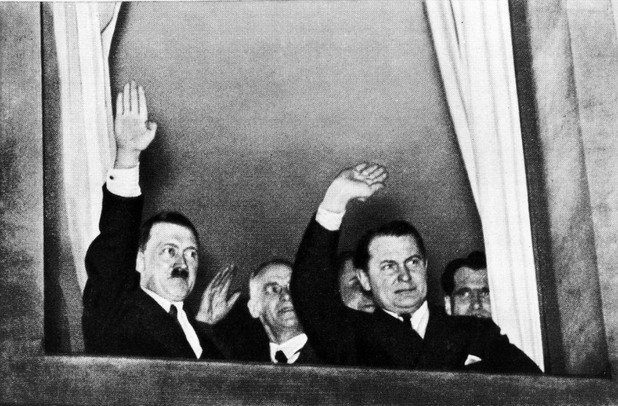 Един мъж е излишен: лицето му се разпознава ясно вдясно до завеса. Рудолф Хес, секретарят на Фюрера, може да стои съвсем близо до своя идол - денят е 30 януари 1933 - датата, на която Хитлер взима властта. Няколко години по-късно …