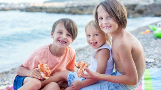 Sweet toddler child, eating pizza on the beach, having fun, smiling happily, kid enjoying dinner