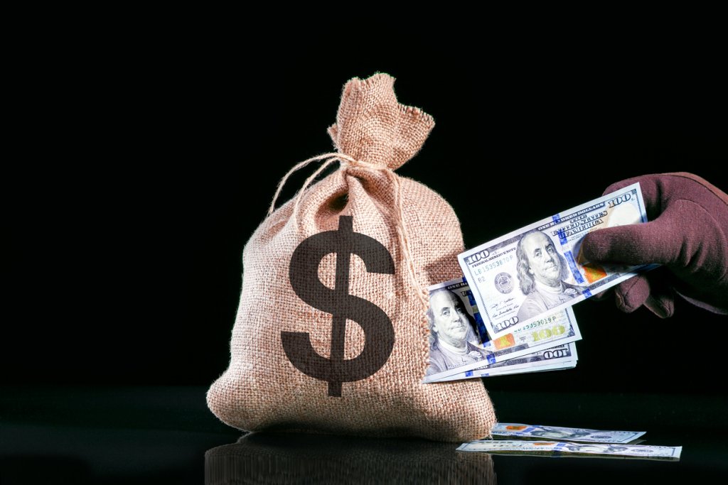 Hand pulls money, dollars out of the bag. Stealing money