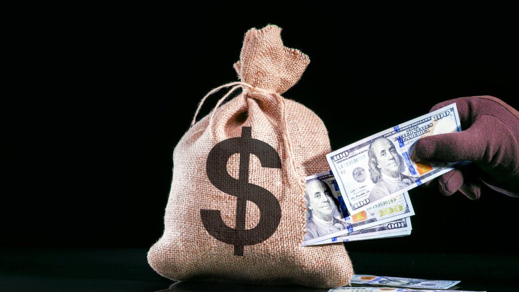 Hand pulls money, dollars out of the bag. Stealing money