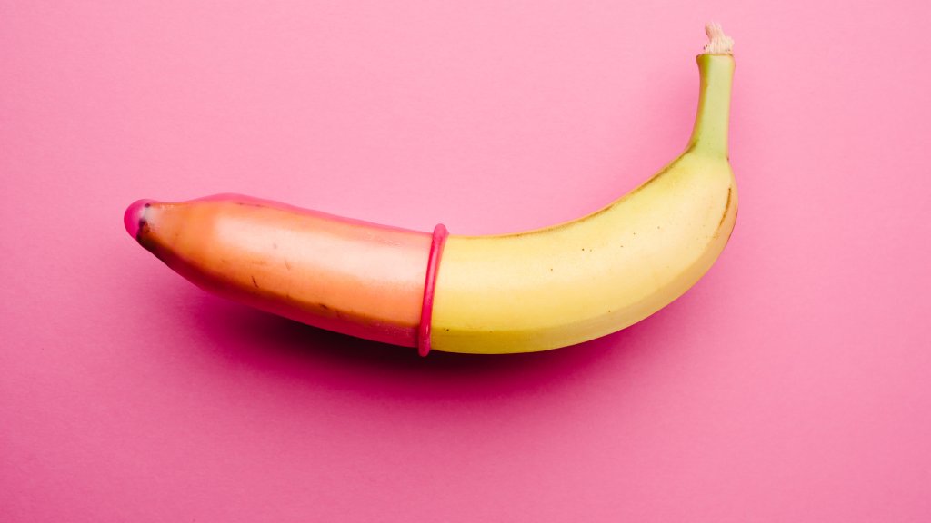 Pink condom on banana in front of pink background