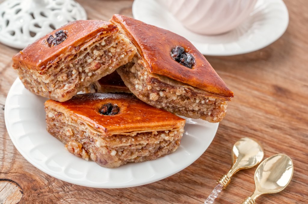 Айле сладкишЗапочваме този богат сладкиш, като си приготвяме захарен сироп от 3 чаши вода и 3 чаши захар с малко лимонов сок и лимонова кора. Оставяме да се охлади. През това време слагаме корите в намаслена тава по следния начин – вадим кора, нагъваме я на хармоника и редим. Поръсваме с малко разтопено масло.
След това приготвяме кексова смес от чаша кисело мляко, чаша брашно, чаша захар, три яйца, пакетче бакпулвер, малко олио и лъжица какао. Заливаме корите за баница, печем на 180 градуса до покафеняване на целия сладкиш и още горещия десерт заливаме със студения сироп. Сервираме добре охладен.