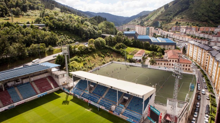 Стадион "Ипуруа" не изглежда най-приятното място да гостуваш. Закачено на хълма край града, мястото е за 5250 зрители, със схлупени трибуни и блокове, надничащи над тях. Тук всичко е малко - Ейбар е 27-хилядно баско градче, но вече втори сезон поред е в елита на испанския футбол.